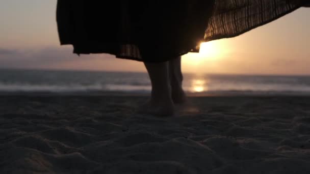 Крупним планом жіночі ноги в чорній спідниці максі, босоніж ходить по піску в океан, перетворюючись на панораму на сонце, що відображає воду — стокове відео