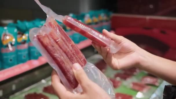 Vergelijking van twee verpakkingen van rij biologische vleesworst in vacuümverpakkingen in handen van de supermarkt — Stockvideo