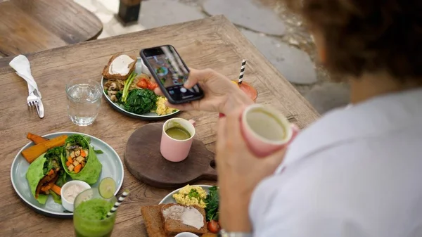 Back of a girl taking photos of her amazing healthy meal to share online. Vegan wraps, plant based breakfast and matcha latte as a part of clean diet — Stockfoto