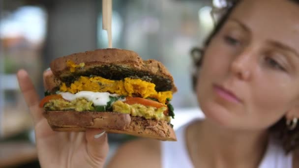 Wanita muda lapar memegang di tangan dan melihat sandwich vegan lezat nya — Stok Video