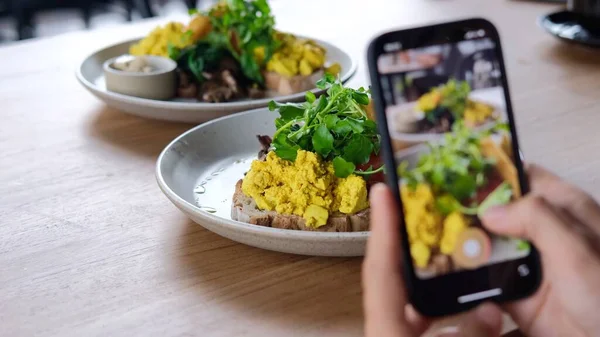 Lifestyle blogger spijkers video 's en foto' s van verse ochtend toastjes met roerei voor social media content in een cafe — Stockfoto