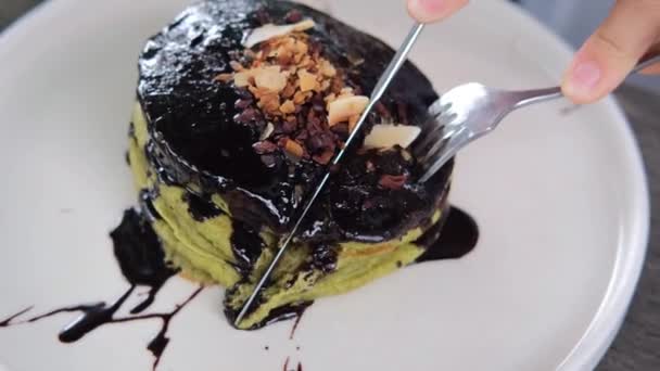 Close-up van menselijke handen snijden lekker gezond veganistisch pannenkoeken met biologische zwarte chocolade op de plaat — Stockvideo