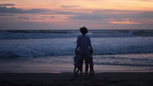 Прекрасный семейный отдых, силуэт матери-одиночки с двумя малышами, бегущими от огромных океанских волн на закате — стоковое видео