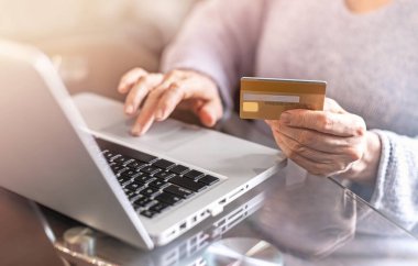 Kredi kartı tutan ve dizüstü bilgisayar kullanan bir yetişkinin elleri. Online alışveriş kavramı