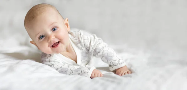 快乐的小女婴微笑着躺在床上 躺在一张白色的床单上 看着家里的相机 复制文字空间 — 图库照片