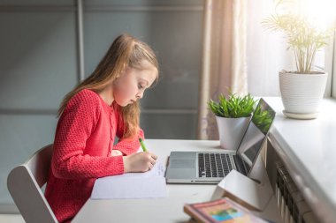 Sevimli küçük kız evde online eğitim, evde öğrenim ve internet iletişimi için dizüstü bilgisayar kullanıyor. Çocuklar uzaktan öğreniyor. Sosyal mesafe. Evde kal..