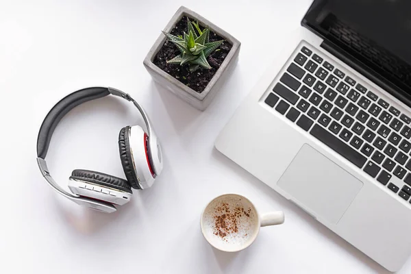 Laptop bilgisayarı, yeşil santral, kablosuz kulaklık ve beyaz fonda kahve olan beyaz iş masası. Serbest çalışan, internetteki iş, online eğitim. Üst manzara, düz uzanma