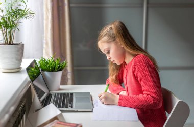 Sevimli küçük kız evde online eğitim, evde öğrenim ve internet iletişimi için dizüstü bilgisayar kullanıyor. Çocuklar uzaktan öğreniyor. Evde kal..