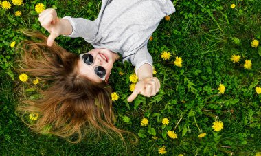 Mutlu küçük bir kız yazın yeşil çimlerde gülümser. Çocuk ellerini zevkle gösteriyor. Çocuklar Günü 'nde. Güzel bir kızın portresi başparmak işareti gösteriyor.