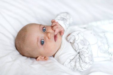 A little baby lying on the bed on a white sheet at home. Close up portrait of newborn baby looking at camera clipart