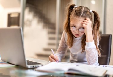 Evde dizüstü bilgisayar kullanarak online öğrenim görmekten ve ödev yapmaktan sıkılmış liseli kız. Evde eğitim ve uzak eğitim