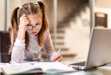Evde dizüstü bilgisayar kullanarak online öğrenim görmekten ve ödev yapmaktan sıkılmış liseli kız. Evde eğitim ve uzak eğitim