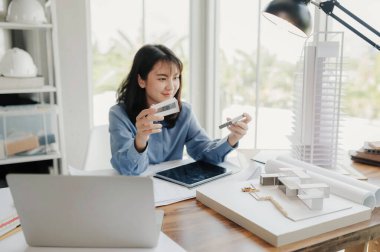 Seçici odak, Asyalı kadın mimar veya mühendis modern apartman daireleri tasarlamak için materyalleri değerlendiriyor. Asyalı kadın mimar ya da mühendis ofiste otur ve analiz et, tasarım projeleri