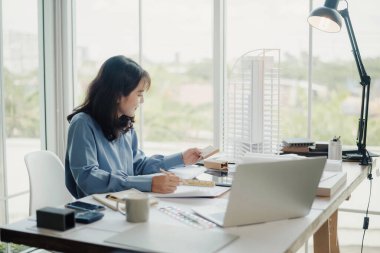 Seçici odak, Asyalı kadın mimar veya mühendis modern apartman daireleri tasarlamak için materyalleri değerlendiriyor. Asyalı kadın mimar ya da mühendis ofiste otur ve analiz et, tasarım projeleri