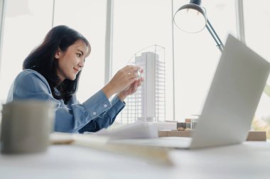 Seçici odak, Asyalı kadın mimar veya mühendis modern apartman daireleri tasarlamak için materyalleri değerlendiriyor. Asyalı kadın mimar ya da mühendis ofiste otur ve analiz et, tasarım projeleri