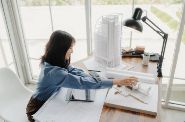 Seçici odak, Asyalı kadın mimar veya mühendis modern apartman daireleri tasarlamak için materyalleri değerlendiriyor. Asyalı kadın mimar ya da mühendis ofiste otur ve analiz et, tasarım projeleri