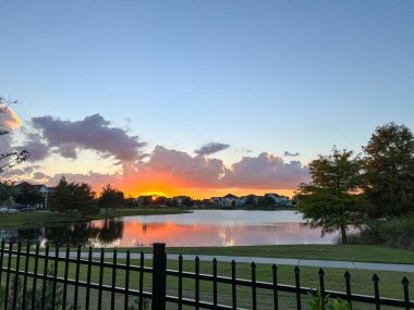 Güzel pembe, turuncu ve mavi gün batımı bir banliyö gölünde yansıyor..