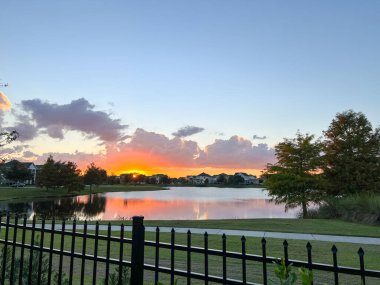 Güzel pembe, turuncu ve mavi gün batımı bir banliyö gölünde yansıyor..