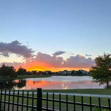 Güzel pembe, turuncu ve mavi gün batımı bir banliyö gölünde yansıyor..