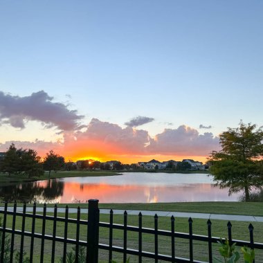 Güzel pembe, turuncu ve mavi gün batımı bir banliyö gölünde yansıyor..