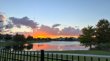 Güzel pembe, turuncu ve mavi gün batımı bir banliyö gölünde yansıyor..