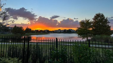Güzel pembe, turuncu ve mavi gün batımı bir banliyö gölünde yansıyor..