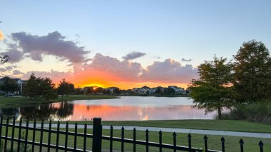 Güzel pembe, turuncu ve mavi gün batımı bir banliyö gölünde yansıyor..