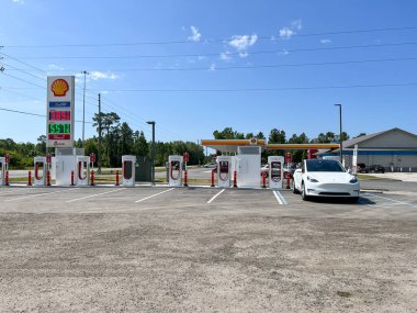 Jasper, FL, ABD-30 Nisan 2022: Florida 'da bir Tesla Supercharger istasyonunda yüksek benzin fiyatlı bir benzin istasyonunun yanında çalışan bir Tesla arabası.