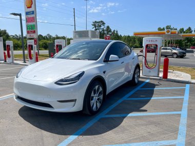 Jasper, FL, ABD-30 Nisan 2022: Florida 'da bir Tesla Supercharger istasyonunda yüksek benzin fiyatlı bir benzin istasyonunun yanında çalışan bir Tesla arabası.