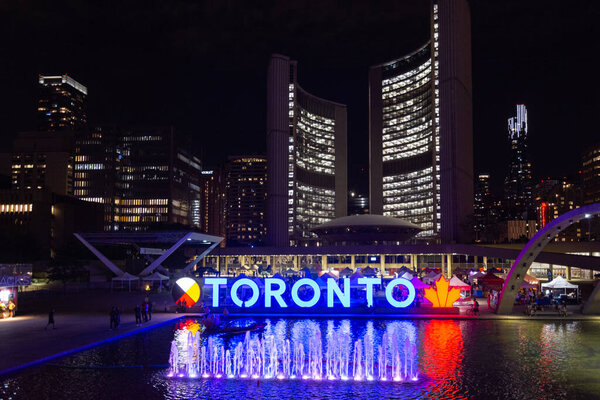 Торонто, Канада - 5 августа 2022: Торонто знак освещается ночью, на Натан Филлипс-сквер виден с Торонто мэрии в фоновом режиме 
