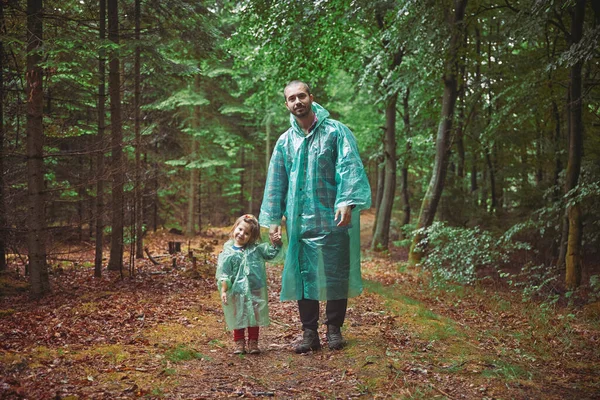 Father and daughter in raincoats walk in the evening forest.