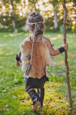Cute baby dressed in the clothes of primitive people with combat staff. 