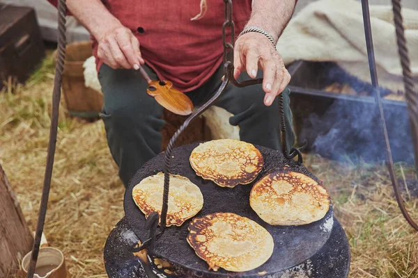 Kamp ateşinde tavada krep kızartan yaşlı adam..