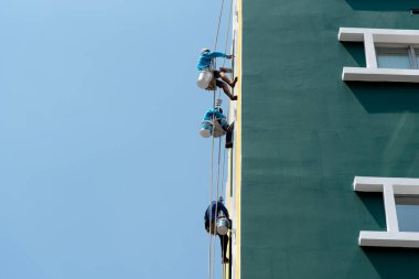 Bangkok, Tayland - 23 Nisan 2017: Tanımlanamayan Asyalı inşaat ressamı bakım ve onarım için duvarda boyamak üzere güvenli bir iple binaya tırmanıyordu