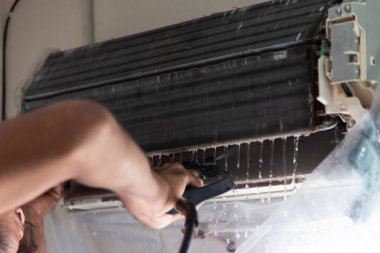 Bakım hizmeti sırasında müşteri evindeki duvardaki tozu temizlemek için havalandırma soğutucusunu suyla temizleyen işçiden işçiye.