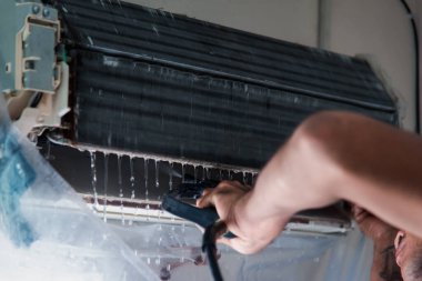 Bakım hizmeti sırasında müşteri evindeki duvardaki tozu temizlemek için havalandırma soğutucusunu suyla temizleyen işçiden işçiye.