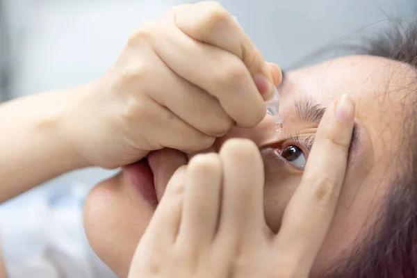 アジアの女性は 目の健康のための眼球の炎症や乾燥問題治療のために目に落ちることによって目のドロップや人工涙を使用します ロイヤリティフリーのストック写真