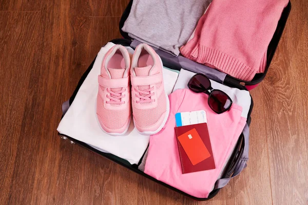 Uma mala aberta com roupas, ténis, óculos de sol. Passaporte, cartão, bilhetes para a viagem. — Fotografia de Stock