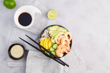 Karidesli kase, avokado, pilav, salatalık, mango, biber ve susam tohumu, gri arkaplanda soya sosu. Hawaii ahi 'si, deniz mahsullü diyet yemeği. Üst görünüm.