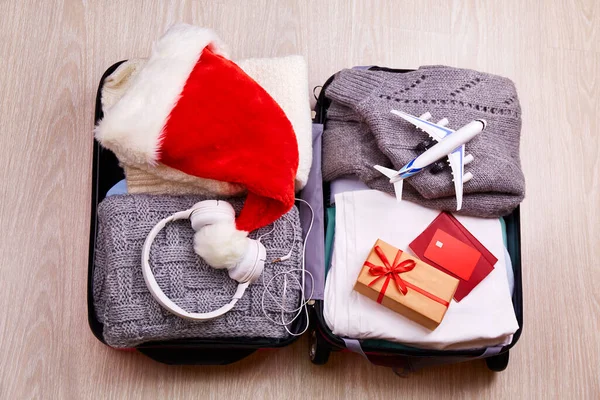 Sıcak kıyafetler, pasaport, kredi kartı, hediye, Noel Baba şapkası ve gelecek Noel tatili için aksesuarlarla dolu açık bir bavul.. 