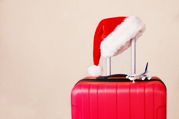 A red suitcase, a Santa Claus hat and a small airplane. The concept of traveling for Christmas and New Year. 