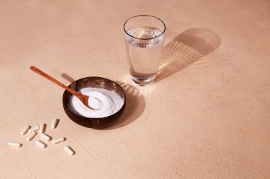 Bir kasede kolajen protein tozu, kapsüller ve bej arka planda bir bardak su. Deri ve eklemler için gıda takviyesi. Yaratıcı fotoğraf.