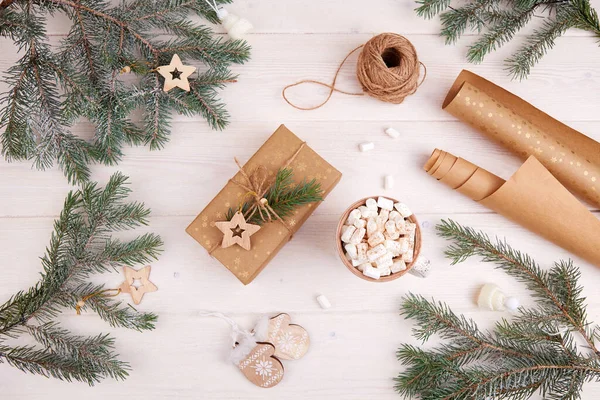 Geschenkverpackung zu Weihnachten. Tannenzweige, eine Tasse Kakao mit Marshmallows, eine Geschenkschachtel, Bastelpapier, Holzspielzeug — Stockfoto