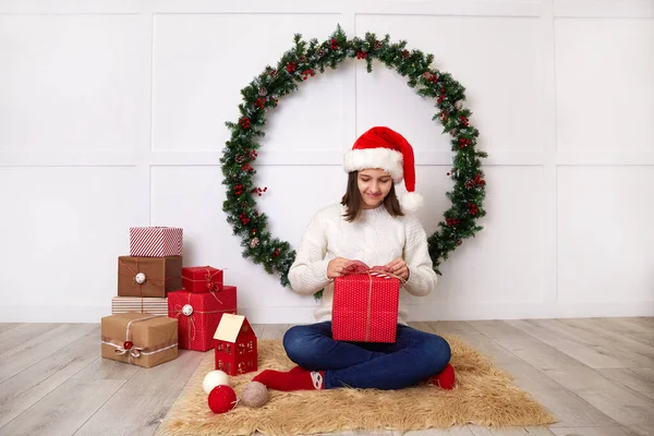 Szczęśliwa dziewczyna w białym swetrze z dzianiny i kapelusz Świętego Mikołaja trzyma pudełko prezentów w rękach. — Zdjęcie stockowe