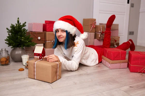 Szczęśliwa dziewczyna w piżamie i kapelusz Mikołaja jest zadowolony z prezentów na Boże Narodzenie. — Zdjęcie stockowe