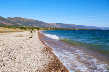 Baykal Gölü, sonbaharın başlarında güneşli bir günde. Dalgalar göl kıyısında.