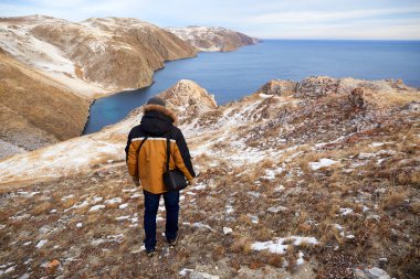 Lake Baikal in December. A man admires the beautiful winter landscape, hiking in nature. Adventures, healthy lifestyle, active recreation, travel concept.