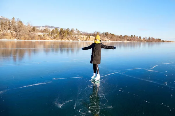 Una jovencita feliz patina sobre el hielo transparente del congelado lago Baikal en un soleado día de invierno. —  Fotos de Stock