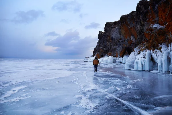Lago congelado Baikal al atardecer. Un viajero masculino camina sobre el hielo transparente del lago. —  Fotos de Stock