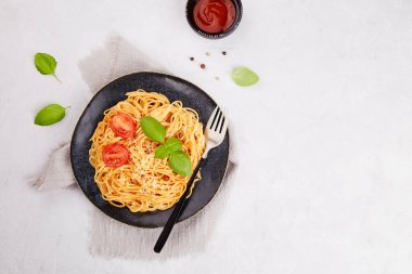 Klasik İtalyan makarnası domatesli, domates soslu, açık gri arka planda koyu tabakta fesleğen. Üst görünüm, alanı kopyala.